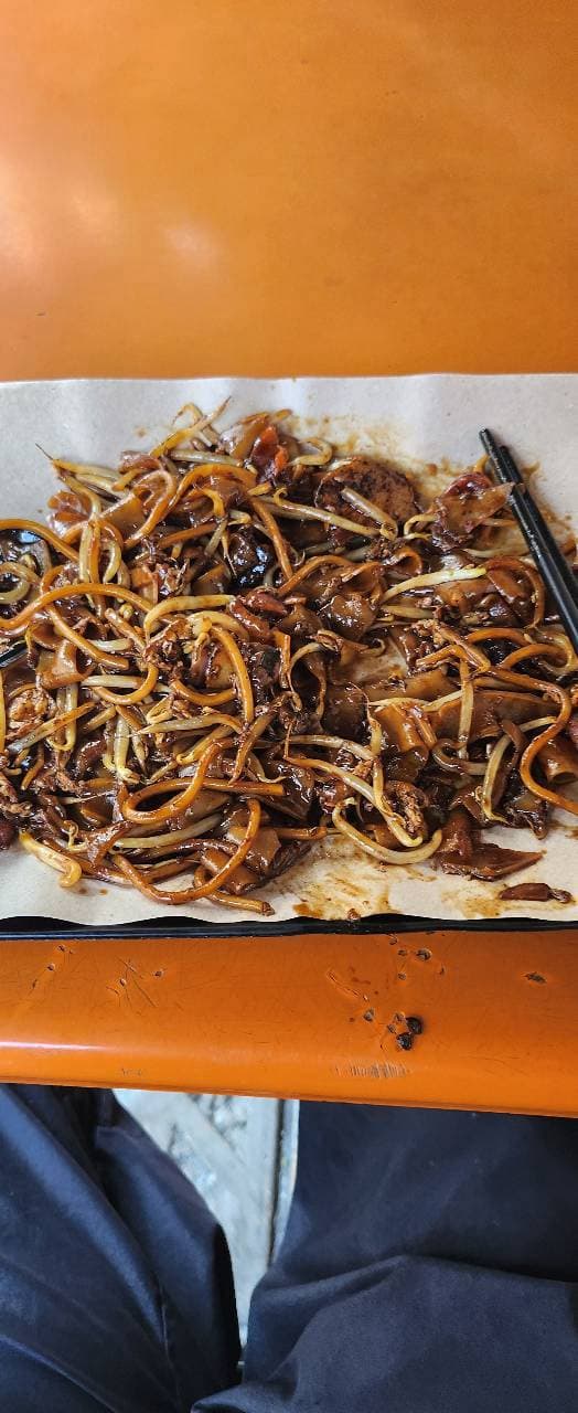 A plate of char kway teow, dark noodles and bean sprouts, on an orange table.